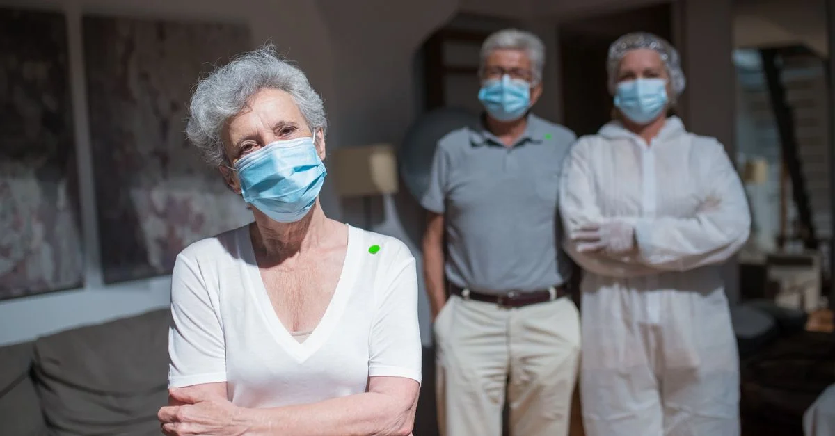 Des travailleurs de la santé en équipement de protection aidant des personnes âgées à l'intérieur, mettant en avant les soins liés à la COVID-19.