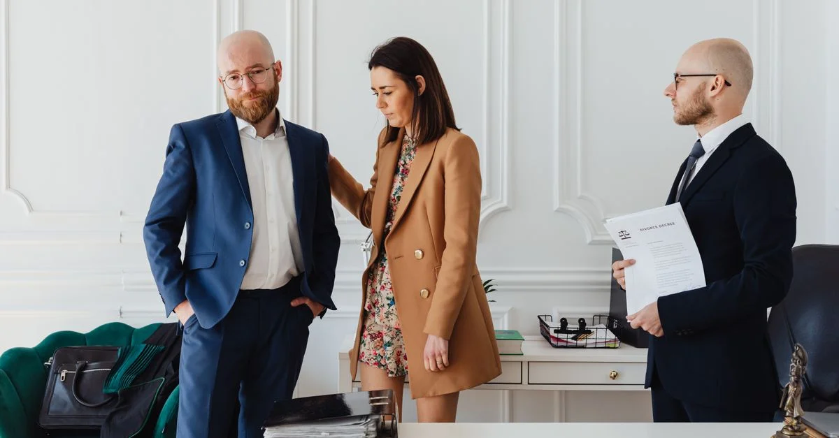 Un couple avec un avocat dans un cadre de bureau, examinant des documents de divorce en tenue formelle.