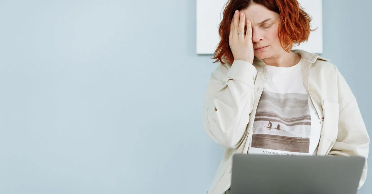 Une femme éprouvant du stress, assise avec un ordinateur portable, se tenant le front.