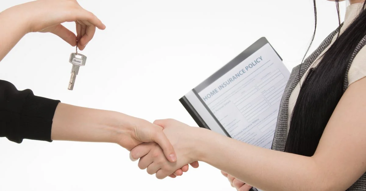 Une transaction immobilière avec une poignée de main et un échange de clés, mettant en valeur un document d'assurance habitation.