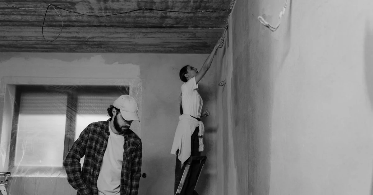 Photo noir et blanc d'un couple peignant une chambre pendant une rénovation de maison.