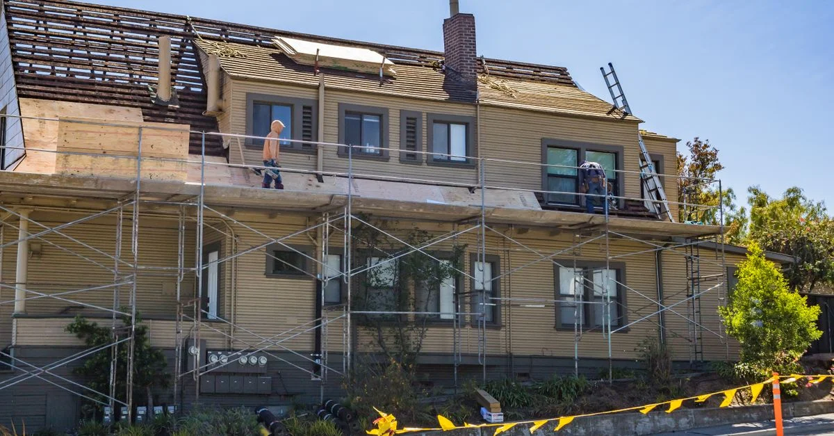 Maison en rénovation avec échafaudages et ouvriers réparant le toit par une journée ensoleillée.