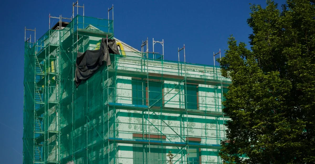 Bâtiment en rénovation couvert d'échafaudages verts contre un ciel bleu clair.