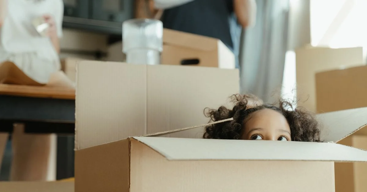 Un enfant jette un coup d'œil hors d'une boîte en carton lors d'un déménagement dans une nouvelle maison, capturant un moment ludique.