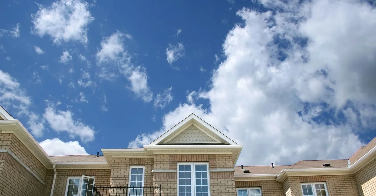 Une maison moderne en briques avec de grandes fenêtres sous un ciel bleu lumineux et des nuages moelleux.