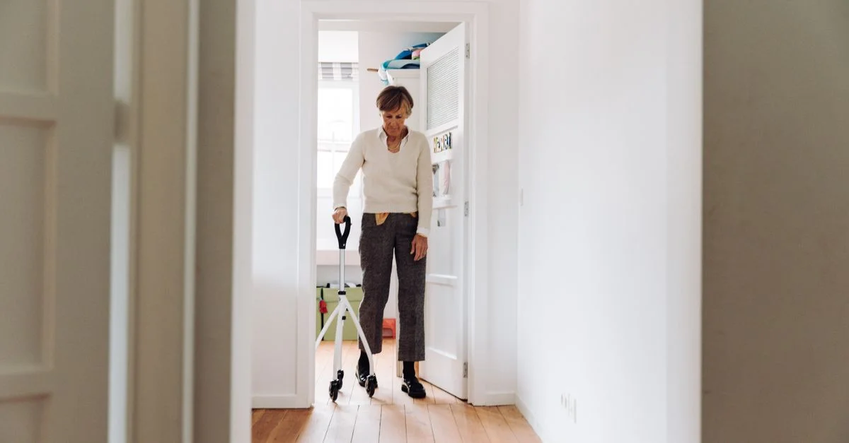 Personne âgée utilisant un rollator dans un couloir ensoleillé, mettant l'accent sur la mobilité et l'indépendance.