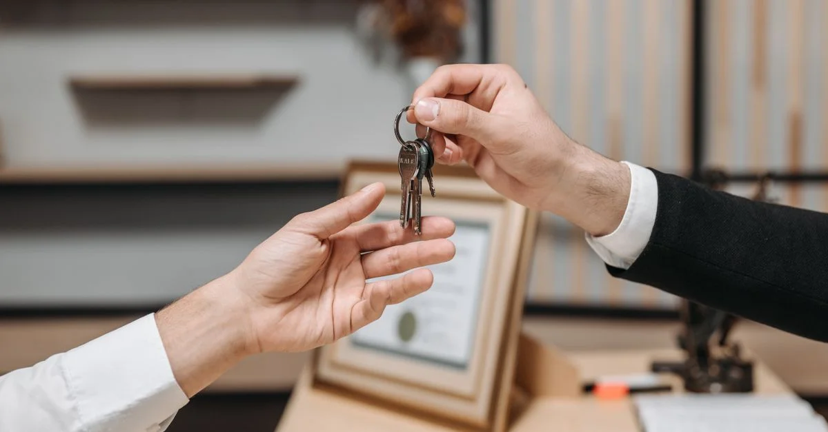 Vue détaillée des mains échangeant des clés dans un environnement de bureaux professionnel, symbolisant les transactions immobilières ou commerciales.