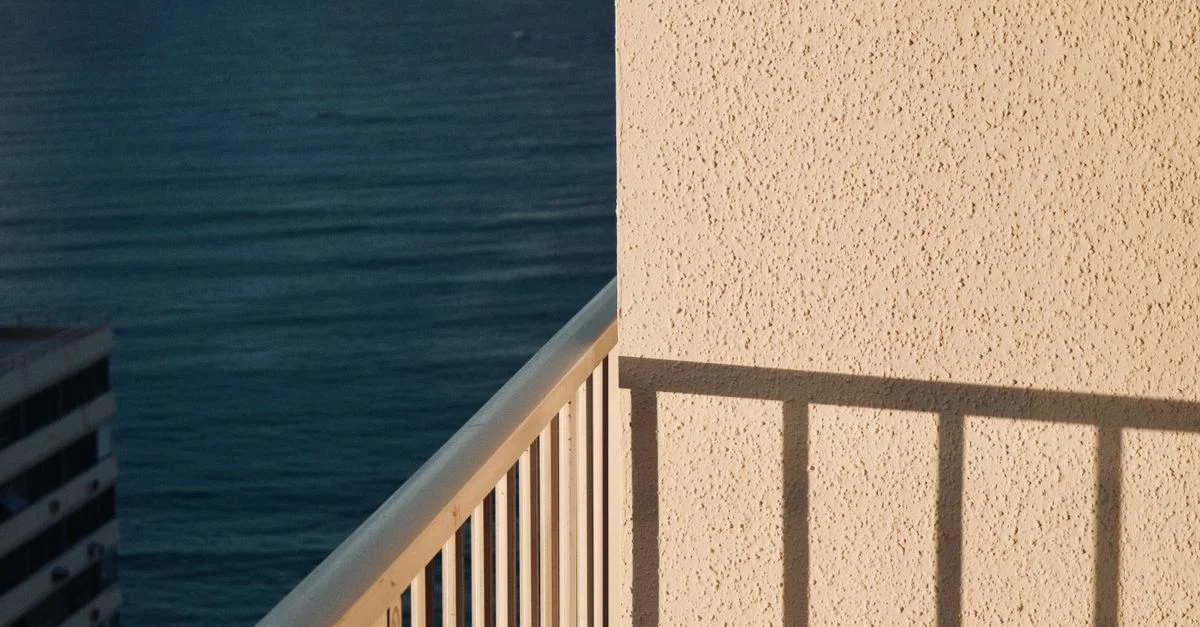 Balcon ensoleillé avec vue sur l'océan à Honolulu, mettant en valeur la tranquillité en bord de mer et les ombres architecturales.